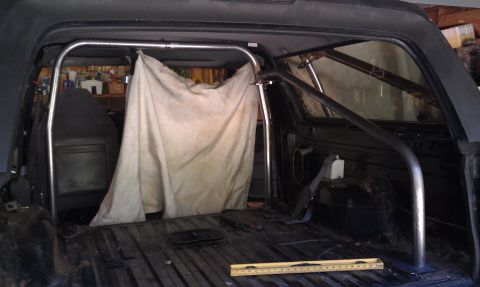 1995 Ford Bronco - Roll cage installation in a 1995 Ford Bronco interior, partially covered by a tarp.