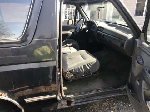 1992 Ford Bronco - The interior of a 1992 Ford Bronco shows wear and tear, including a damaged driver's seat and visible rust.