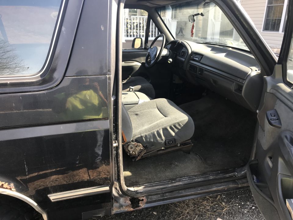 Dark gray 1992 Ford Bronco interior with ripped driver's seat and rust on the door sill