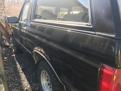 1992 Ford Bronco - This black SUV is seen from the side, with visible rust on the rear fender and a glimpse of the interior seats.