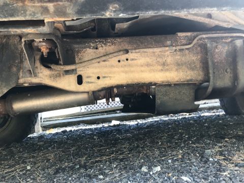 1992 Ford Bronco - The undercarriage of a vehicle shows rust and wear on the frame and exhaust components.