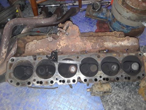 1985 Ford Bronco - Close-up of a rusty engine cylinder head with exhaust manifold, likely for a V8 engine.