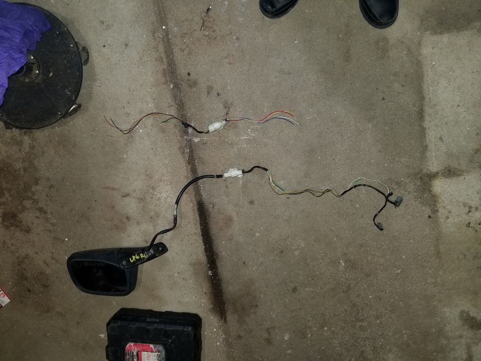 Black car side mirror with wiring harness and loose wires on concrete floor