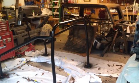 1995 Ford Bronco - Roll cage installed in a garage setting, surrounded by various automotive parts and equipment.
