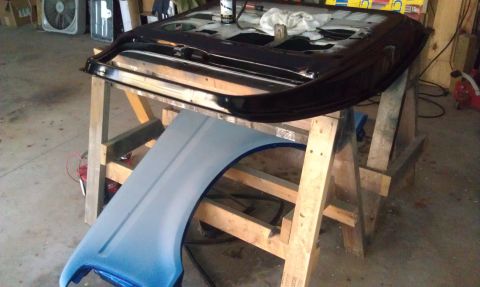1995 Ford Bronco - A black door and a light blue fender are resting on wooden sawhorses, likely for repair or painting.