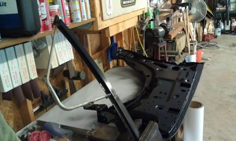 1995 Ford Bronco - A black car door frame is disassembled and laid out on a workbench in a cluttered garage setting.