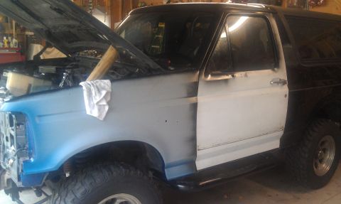 1995 Ford Bronco - This Ford Bronco is in a garage with its hood up, showing primer on the fender and a white door.