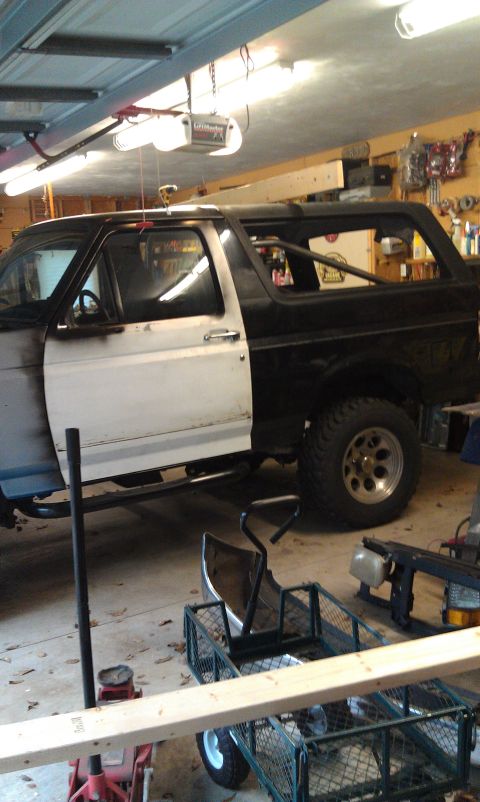 1995 Ford Bronco - A 1995 Ford Bronco is seen in a garage, with its driver's side door open and the body showing a transition from primer to black paint.