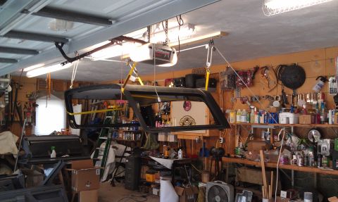 1995 Ford Bronco - A vehicle's hardtop is hoisted in a cluttered garage, surrounded by tools and supplies.