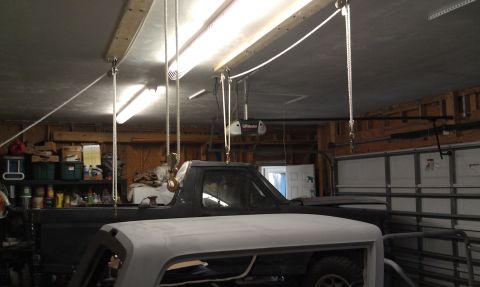 1995 Ford Bronco - A dark truck cab is visible in a garage, with a white hood in the foreground and a garage door in the background.