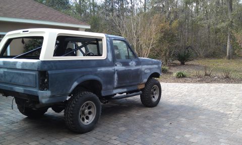 1995 Ford Bronco - A dark blue and white Ford Bronco is parked outdoors, viewed from its side profile.