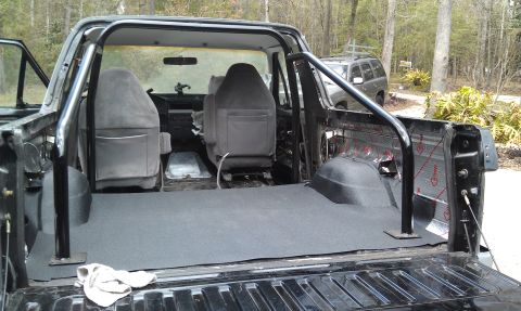 1995 Ford Bronco - The interior of a black Ford Bronco shows grey seats and a roll cage, with a carpeted bed area.