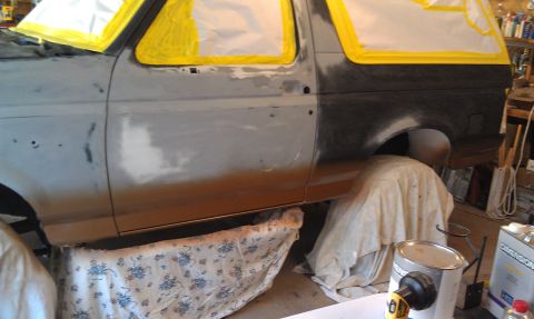1995 Ford Bronco - This Ford Bronco is in a workshop, covered in primer and masking tape, indicating it is being prepped for a new paint job.