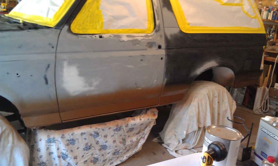 Gray Ford Bronco undergoing bodywork, with yellow masking tape around windows and doors