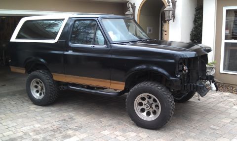 1995 Ford Bronco - This black Ford Bronco features a white top and is lifted with off-road tires, missing its front bumper.