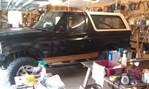 1995 Ford Bronco - A black and tan Ford Bronco is parked in a garage with various tools and supplies around it.