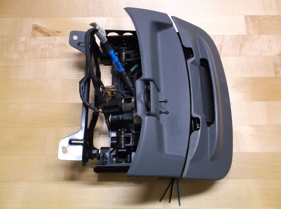 Gray plastic car interior component with exposed wiring and metal bracket, on a wooden surface