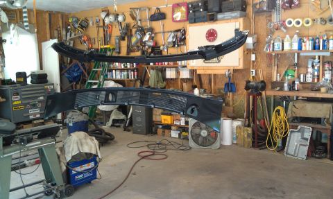 1995 Ford Bronco - Two large black car parts are suspended from the ceiling in a cluttered garage, with tools and supplies visible on the walls and shelves.