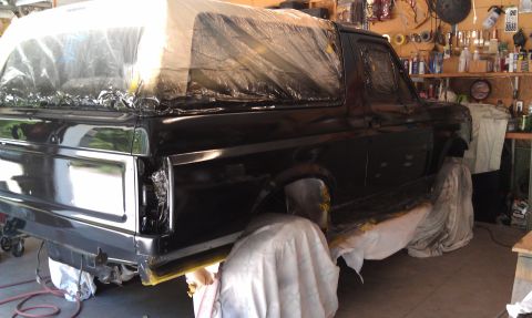 1995 Ford Bronco - A black 1995 Ford Bronco is seen from the side, covered in plastic sheeting as it undergoes a paint job in a garage.