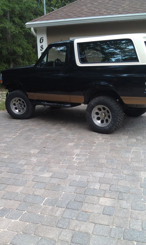 1995 Ford Bronco - This black and tan Ford Bronco is viewed from the side, parked on a paver driveway in front of a house.