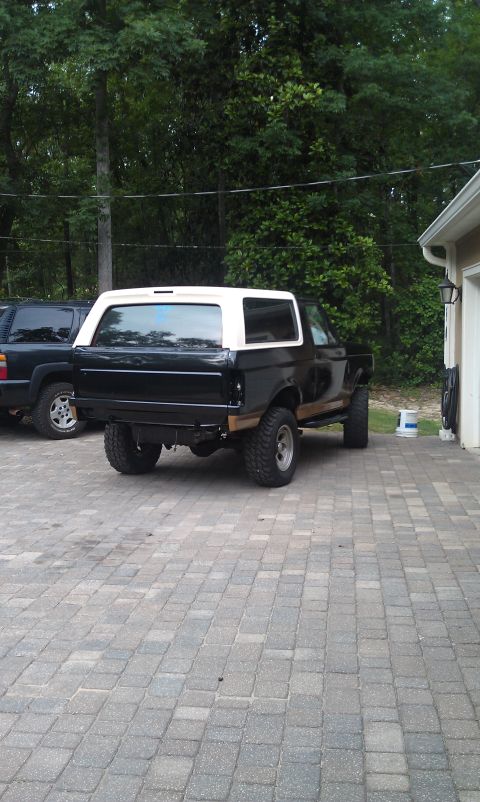 1995 Ford Bronco - Rear view of a black Ford Bronco with a white top, parked on a paver driveway.