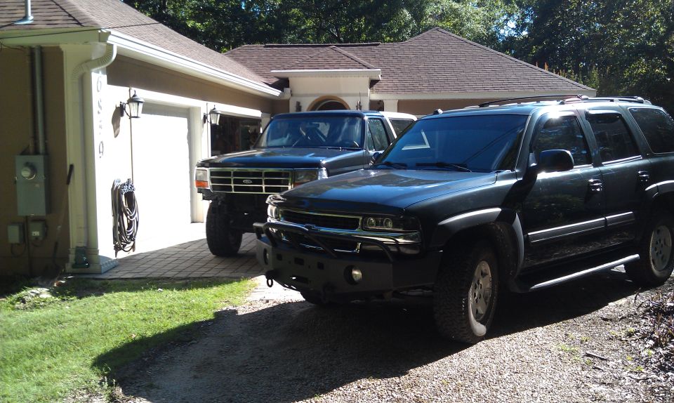 Black 1992 Ford Bronco with lifted suspension and aftermarket bumper parked next to a dark SUV