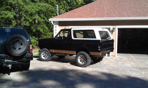 1995 Ford Bronco - A black and white 1995 Ford Bronco is parked next to another SUV in front of a garage.