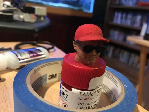 1989 Ford Bronco - A model head wearing sunglasses and a red cap is placed on a red paint bottle, with blue tape around it.