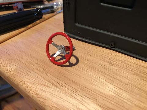 1989 Ford Bronco - A close-up view of a red toy steering wheel with silver accents, resting on a wooden table next to some tools.