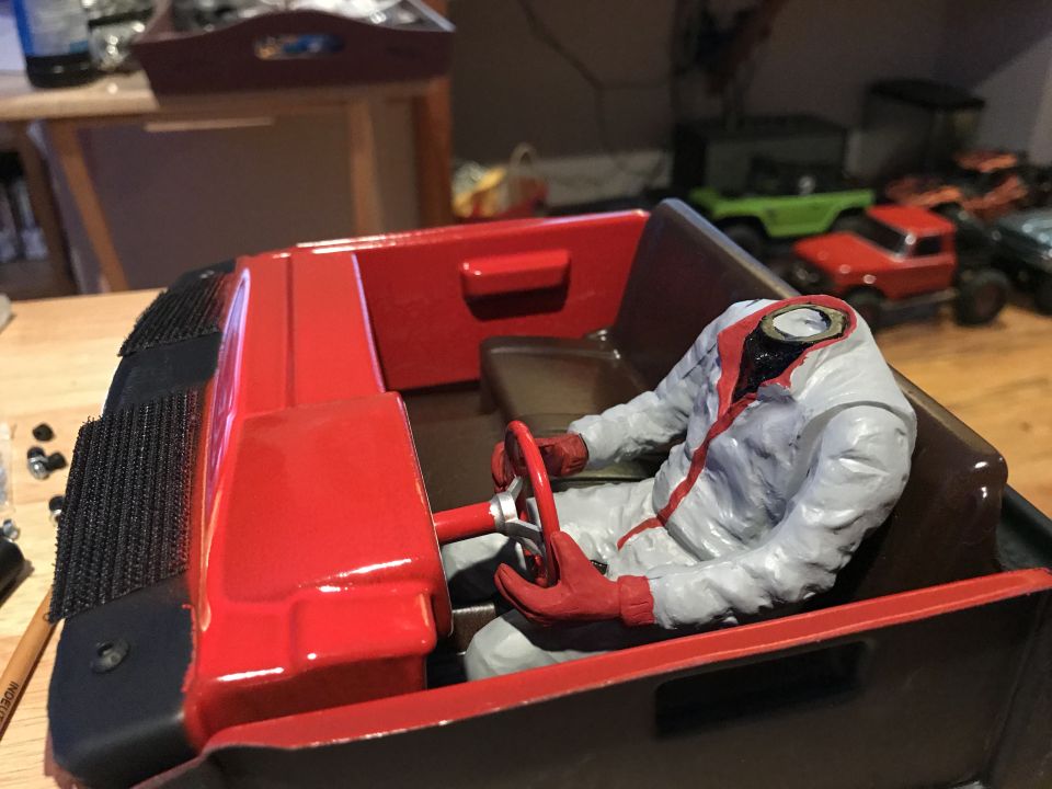 Red and black model car interior with a headless figure in a gray and red racing suit holding a red steering wheel