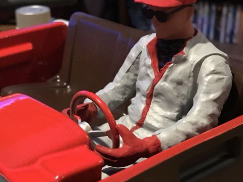 1989 Ford Bronco - A model driver, dressed in a red cap and racing suit, grips the steering wheel of a red vehicle.