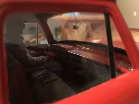 1989 Ford Bronco - A close-up shot of a vehicle's interior, showing a driver figure and fuzzy dice hanging from the rearview mirror.