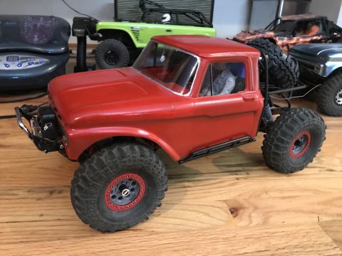 1989 Ford Bronco - A red RC truck sits on a wooden surface with other RC vehicles in the background.