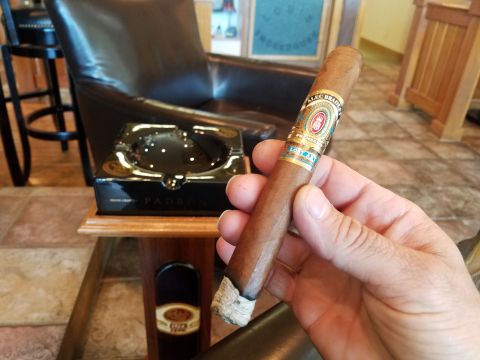 2018 Ford Bronco - A hand holds a cigar, with a leather chair and ashtray visible in the background, suggesting a relaxed setting.