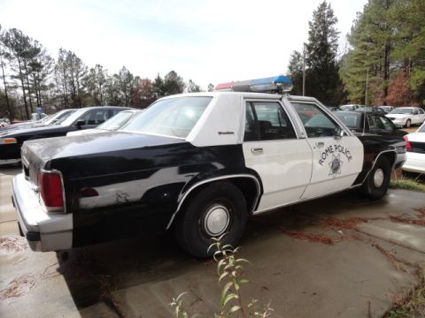 1988 Ford Crown Victoria LTD - A black and white 1988 Ford Crown Victoria LTD police car is parked outdoors next to other vehicles.