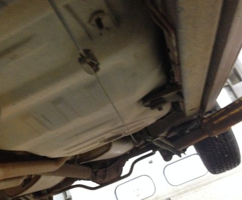1988 Ford Crown Victoria LTD - The underside of a 1988 Ford Crown Victoria LTD reveals its fuel tank, exhaust pipes, and a portion of the rear wheel.