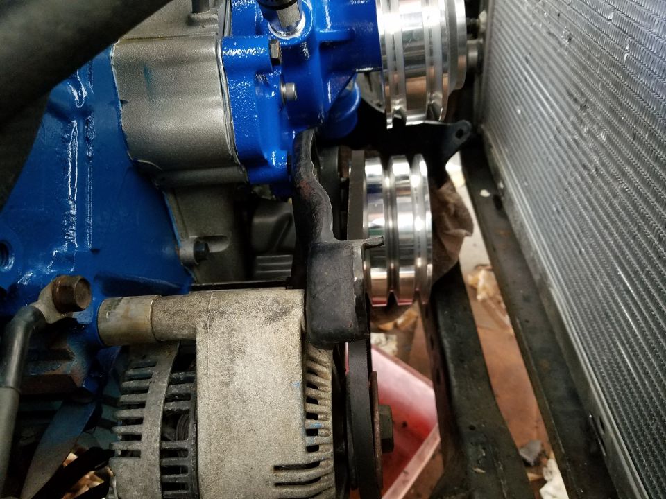 Engine pulleys and alternator with blue painted housing and radiator in background