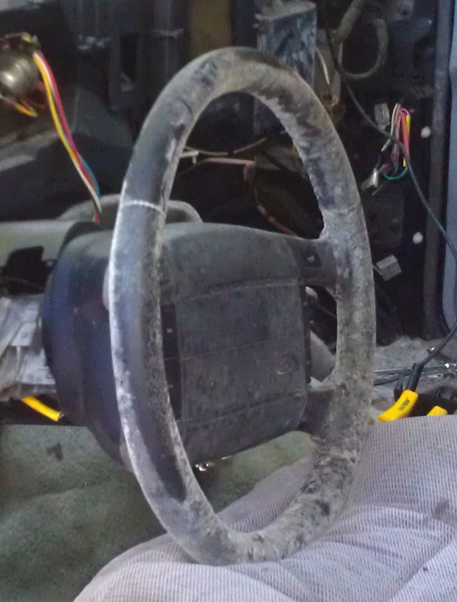 Dusty bare steering wheel with column shroud removed inside a vehicle