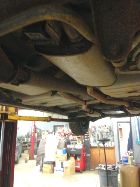 1988 Ford Crown Victoria LTD - A view from beneath a vehicle on a lift, revealing the exhaust system and suspension parts.