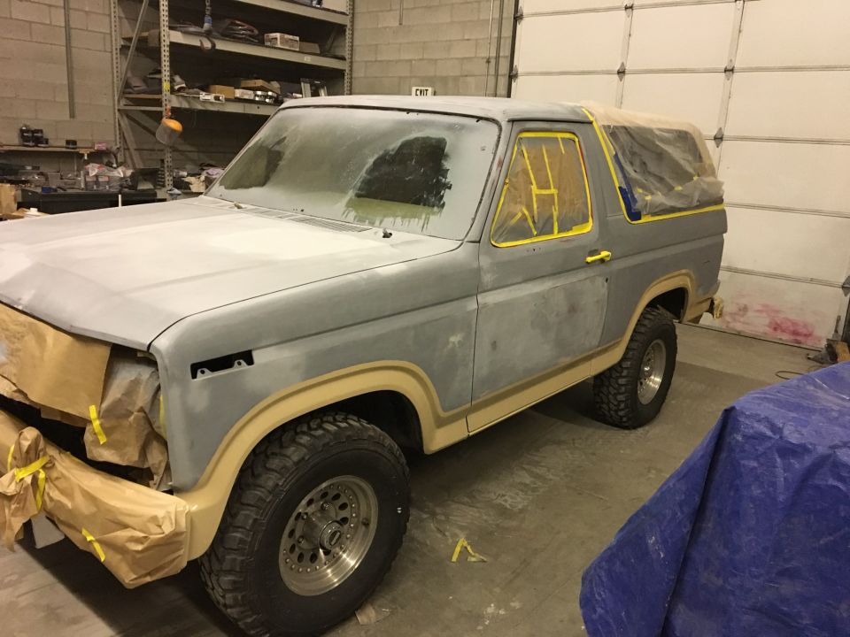 Gray Ford Bronco in a garage, prepped for paint with masking tape and paper covering windows and trim