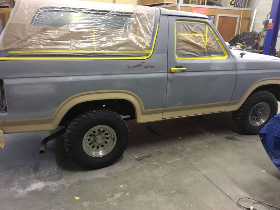 Side view of a gray 1985 Ford Bronco with windows taped off for paint