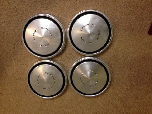Four Ford Motor Company stainless dog-dish hubcaps on tan carpet