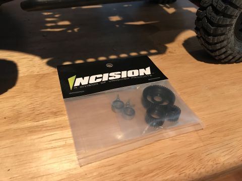1989 Ford Bronco - Packaging for Incision RC car parts, containing gears and screws, is shown on a wooden surface.