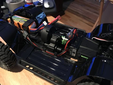 1989 Ford Bronco - Close-up view of an RC car's internal components, including the battery, motor, and wiring, on a wooden surface.