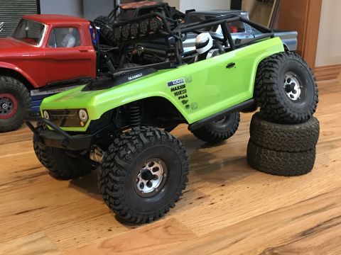 1989 Ford Bronco - A bright green RC rock crawler is positioned with its tires on top of other tires, while a red RC truck sits behind it.