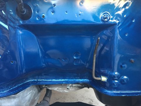 1978 Ford Bronco - The engine bay is painted a vibrant blue, showing various metal parts and a hose attached to the firewall.