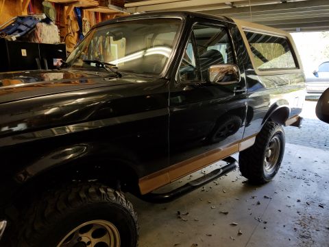1995 Ford Bronco - Side view of a black Ford Bronco with tan accents and aftermarket side steps.