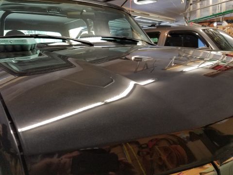 1995 Ford Bronco - A dark SUV's hood shows a dent and is parked next to another vehicle in a garage.