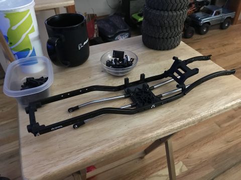 1989 Ford Bronco - RC car chassis and components laid out on a wooden table, with a mug and spare parts visible.