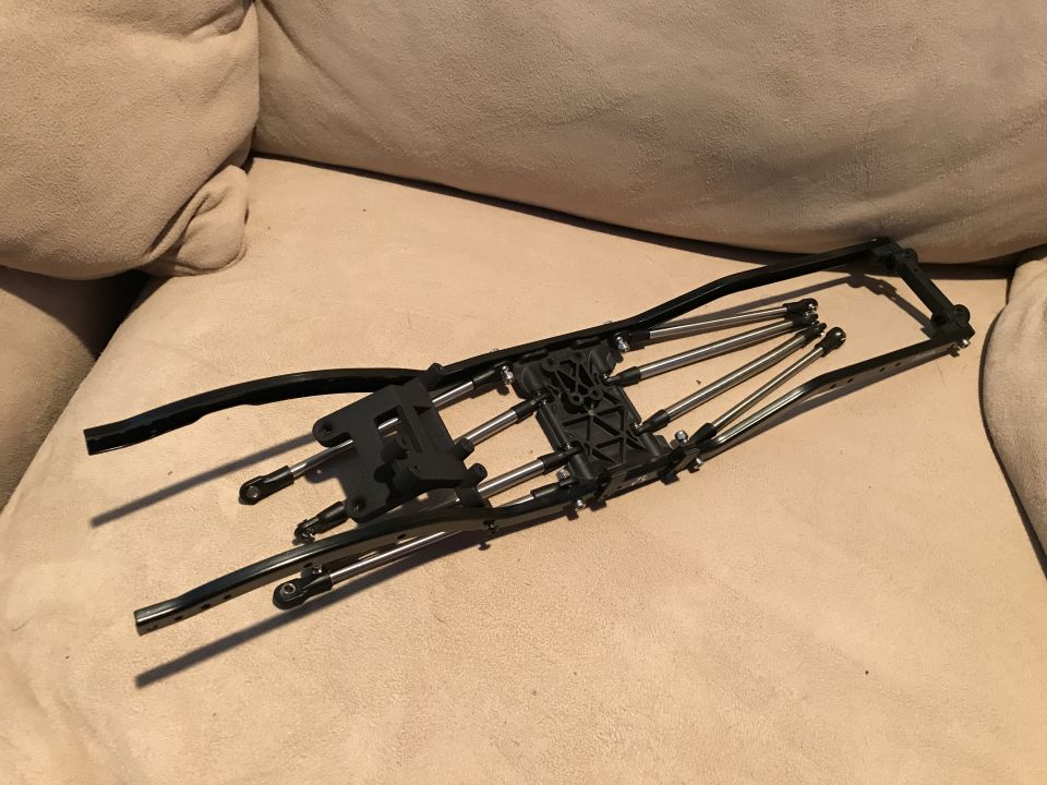 RC car chassis with metal suspension links and black plastic frame components on a beige couch